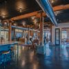 A large, open office space with a kitchen area, with a black ceiling, wooden beams, and a concrete floor.