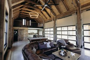 A big, modern living room with a high ceiling, a glass wall, and a cool chandelier